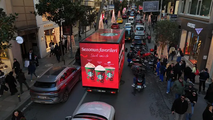 Kalabalık caddede Starbucks reklamı yayınlayan kırmızı LED araç